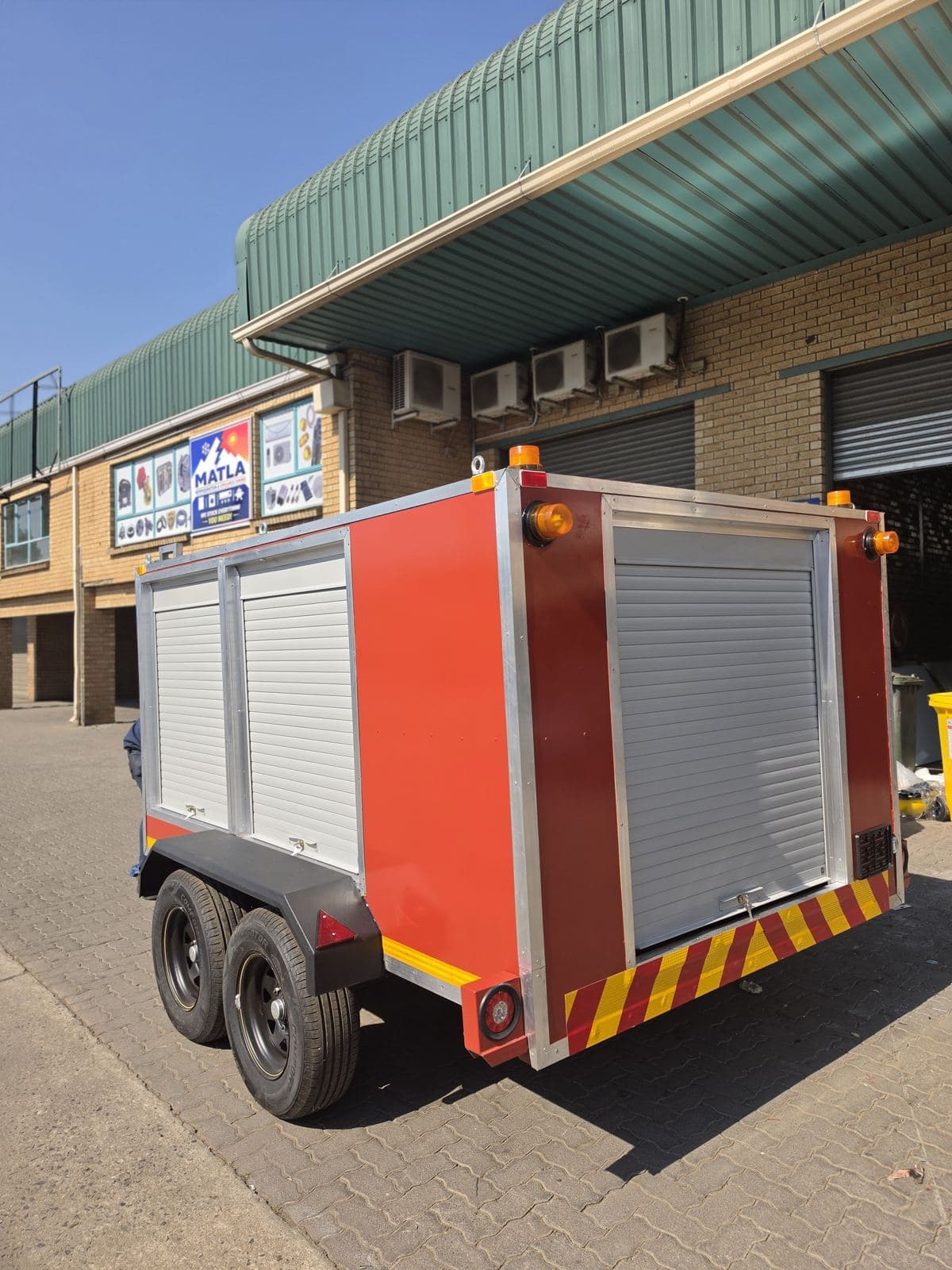 Rear three-quarter view of the finished red hazmat trailer outside the workshop.