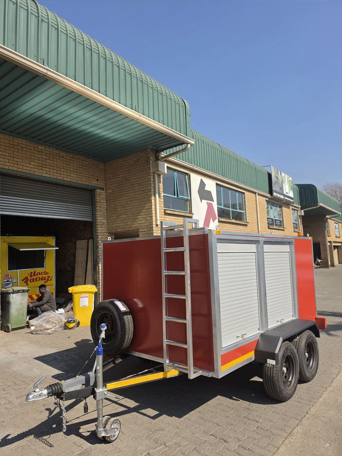 Hazmat trailer parked outside the Trailored workshop, showing the front roof-access ladder and two side roller shutters.