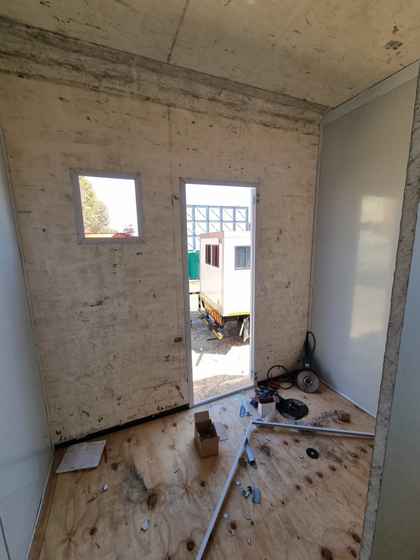 Interior view of window openings cut into the trailer wall, looking out to the yard, with the raw plywood structure still exposed