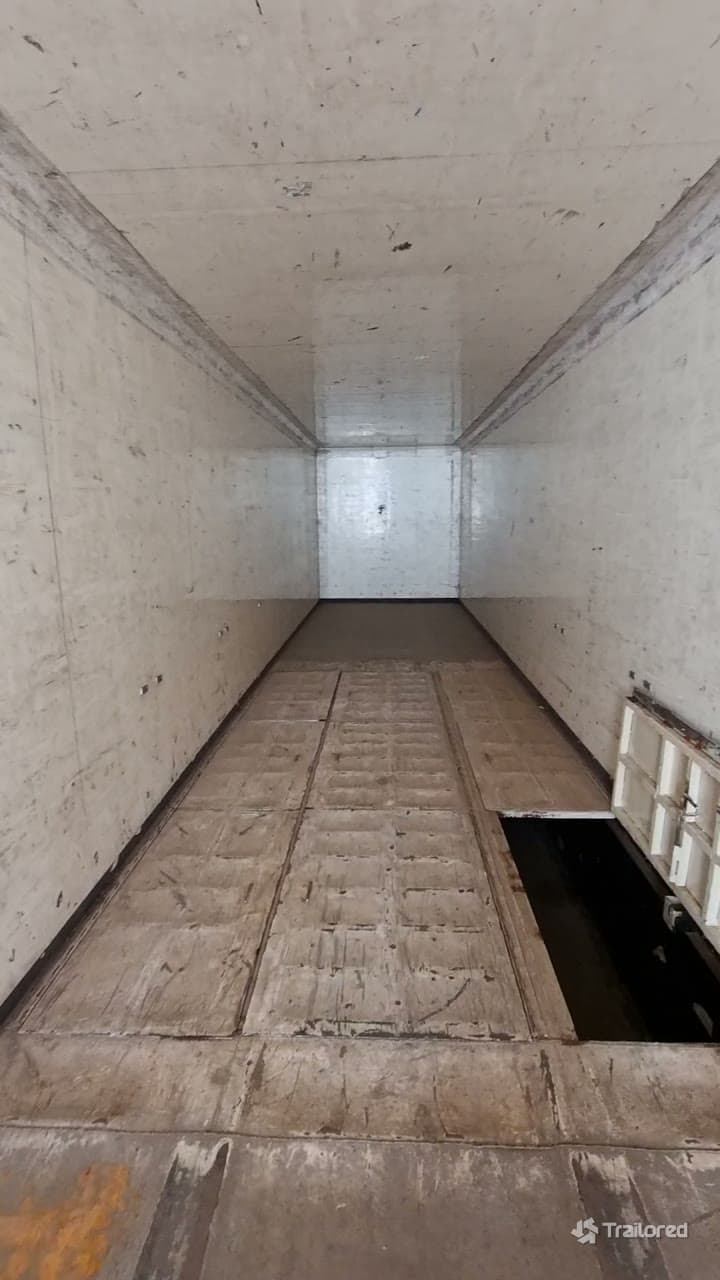 The bare interior of the tautliner before conversion — empty steel walls and a worn timber load floor with the running gear exposed