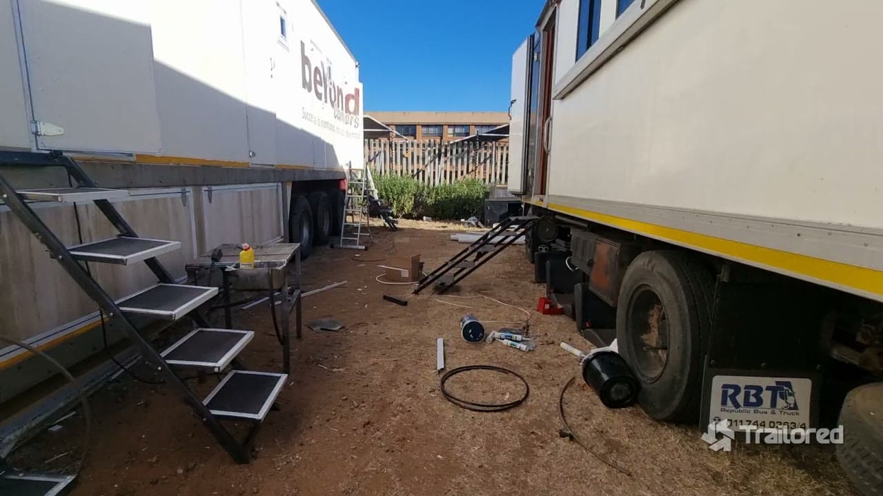 On-site build scene showing fabricated checker-plate access stairs, the awning windows and services being run to the trailer